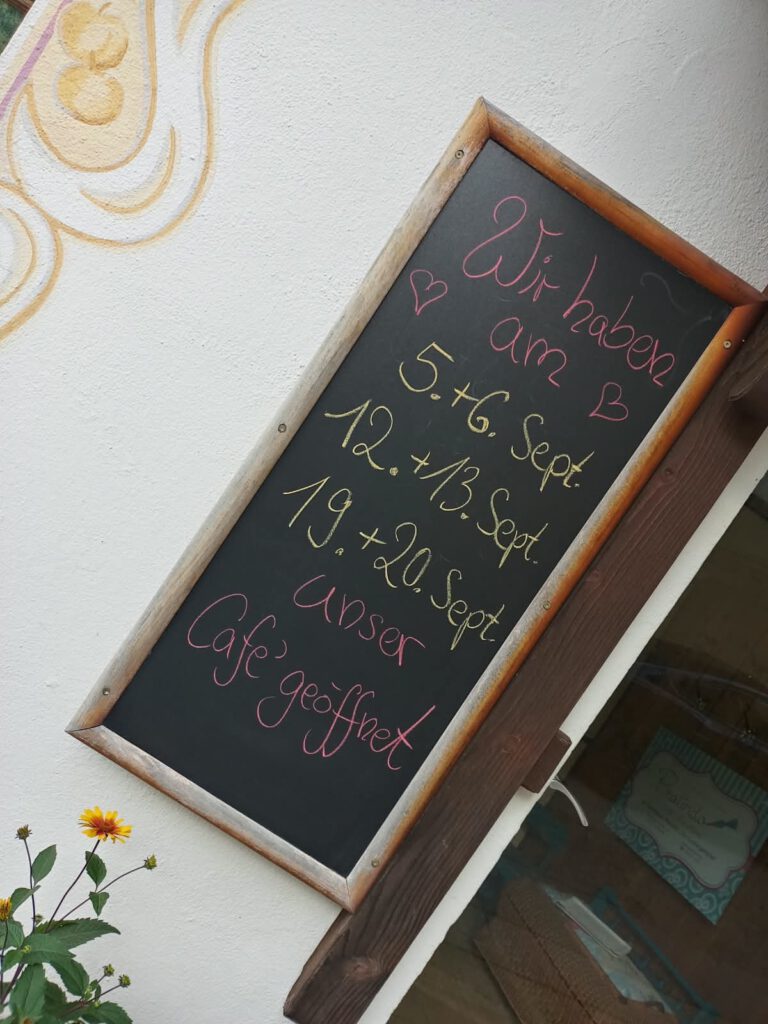 Tafel an Wand mit den Café-Öffnungszeiten von September